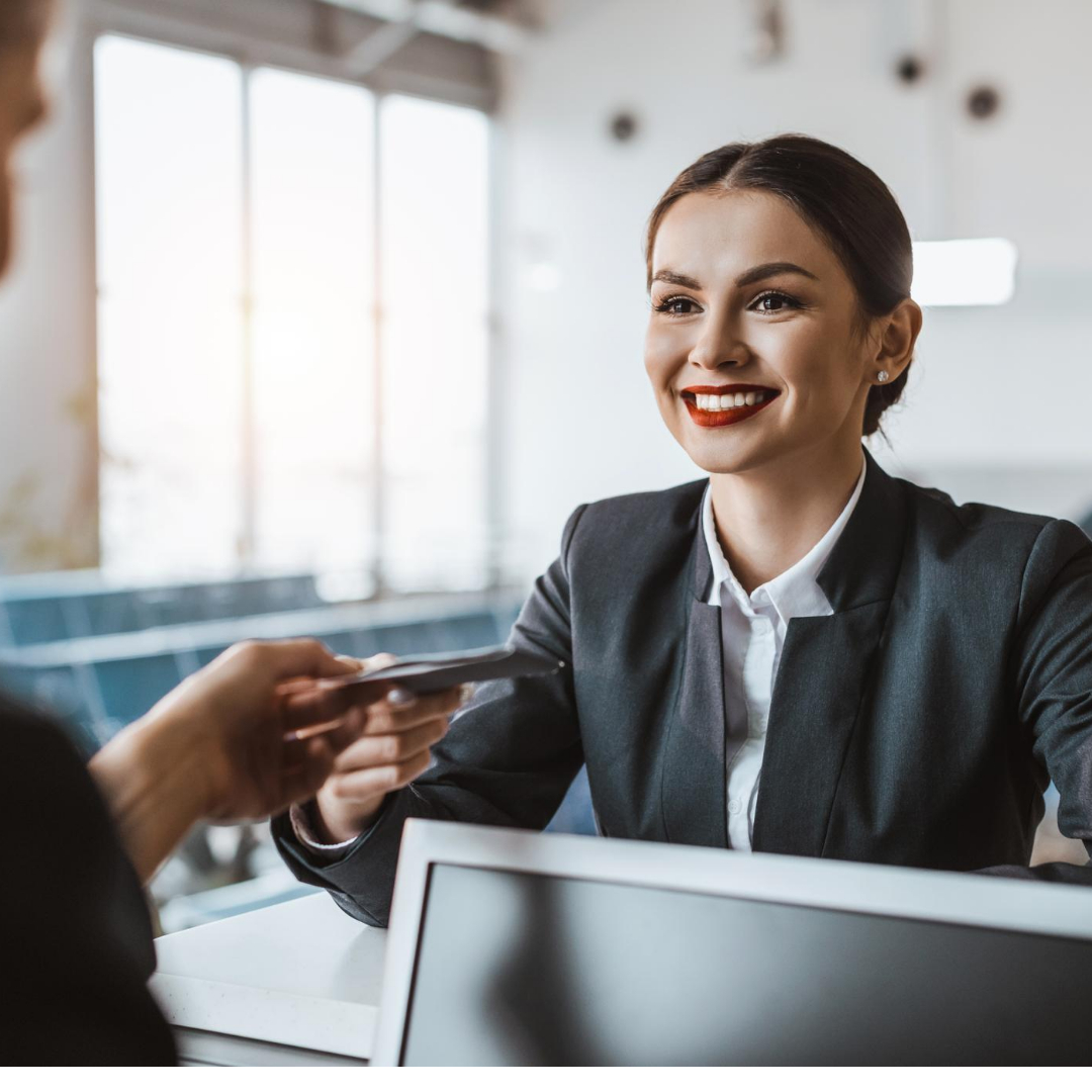 A smiling woman at the front desk handing over something to a man. A smiling woman at the front desk handing over something to a man.